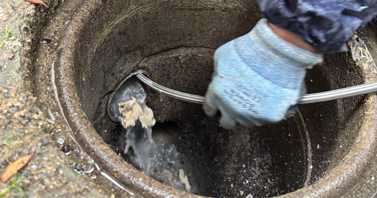 屋外の排水マスから高圧洗浄ホースを入れて排水管を清掃している様子